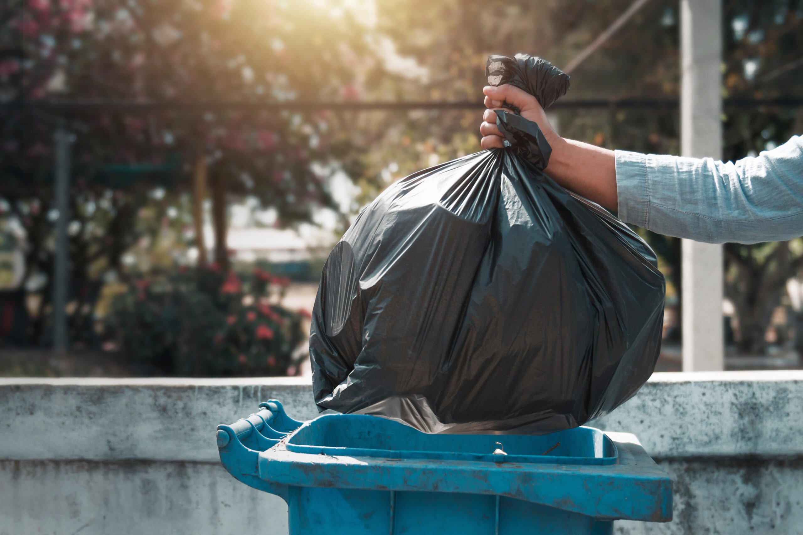 Hand holding garbage black bag putting and putting it into trash 